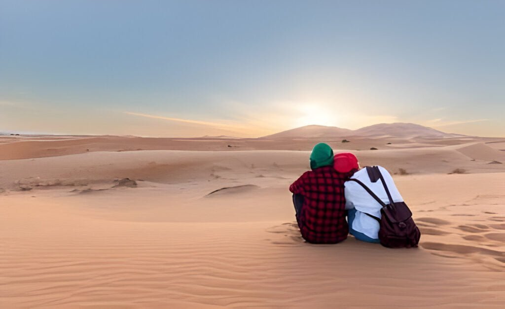 Desert-Sunset-Couple-romantique-assis-jouissant-des-couleurs-chaudes-du-desert-au-coucher-du-soleil-Desert-du-maroc
