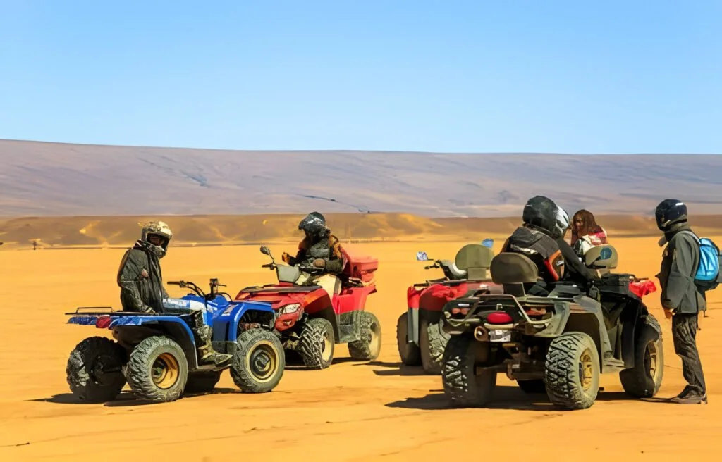 Merzouga Morocco Several riders wait with their quad ATVs in the Sahara Desert The vehicles sit under a blue sky on a flat stretch of sand